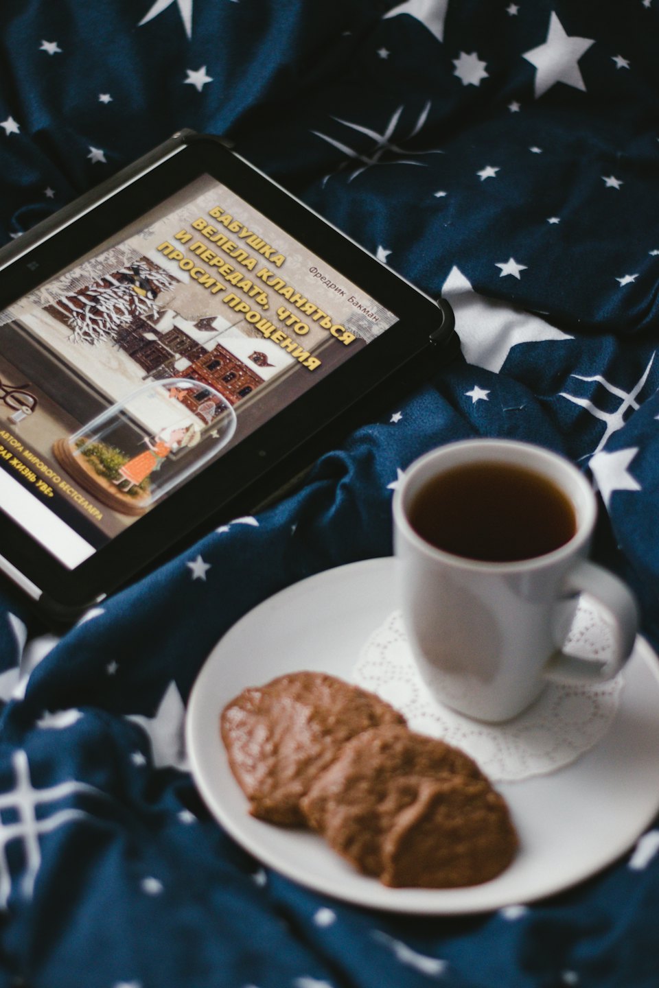 Tablet with e-book on a starry bedspread next to tea and cookies.
